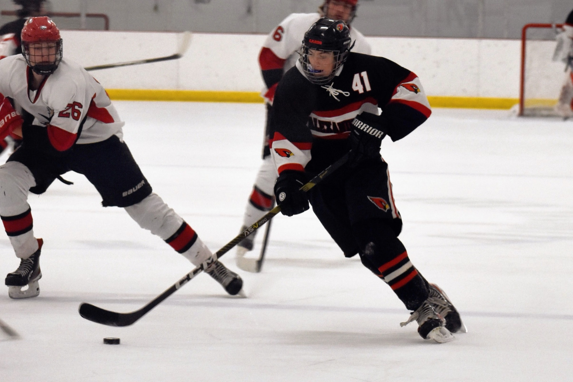 Jackson Drum driving up the ice with the puck in his Alexandria Cardinals jersey